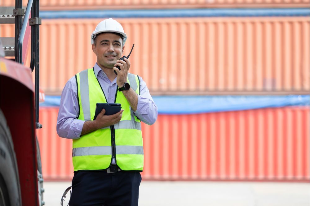 engineer using walkie talkie and tablet for preparing a job beside truck in containers warehouse