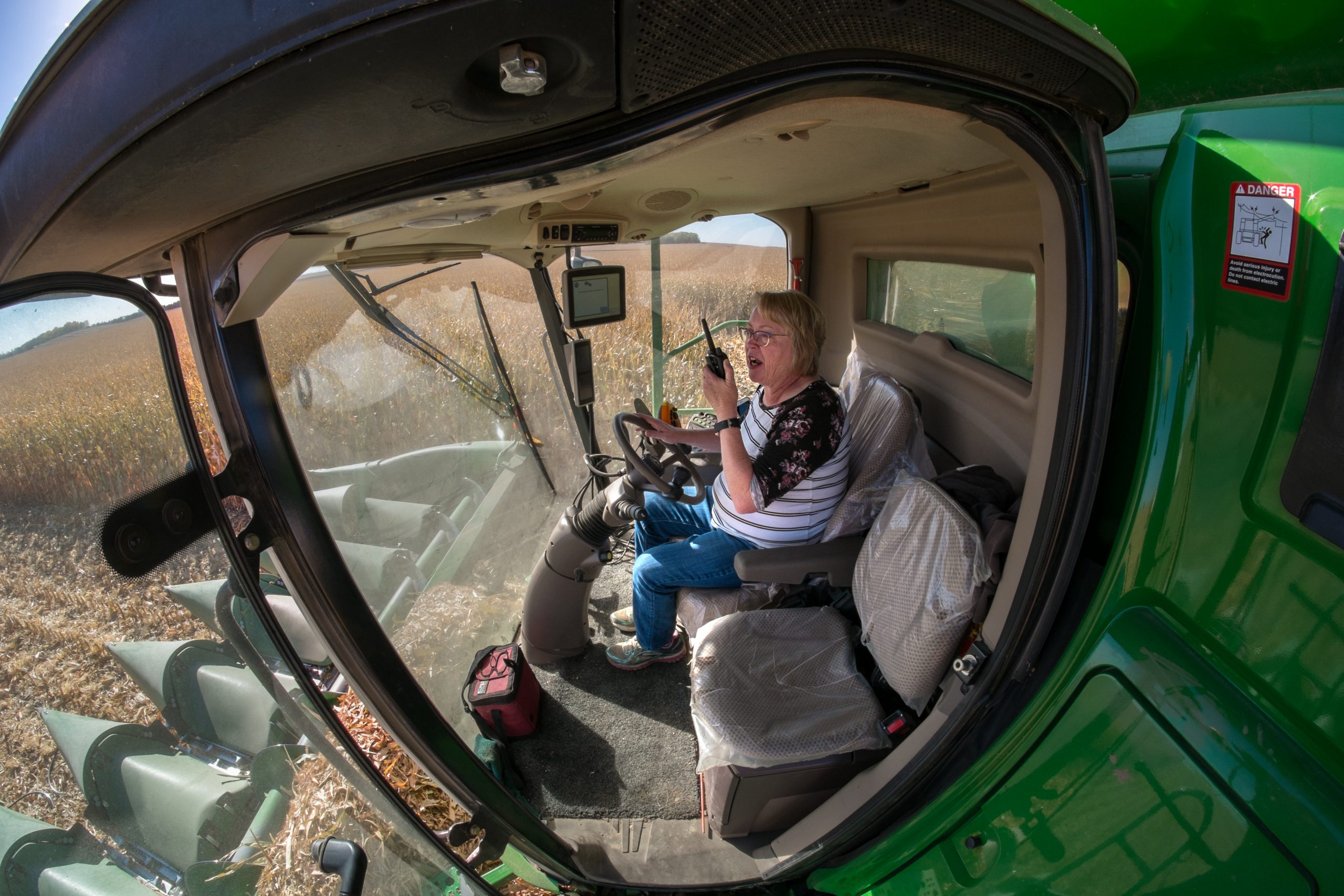 Female farmer using a walkie-talkie whilst driving a combine during harvest